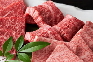 Close-up of raw, thick-cut premium Wagyu beef cubes displaying intense white fat marbling, garnished with green leaves.