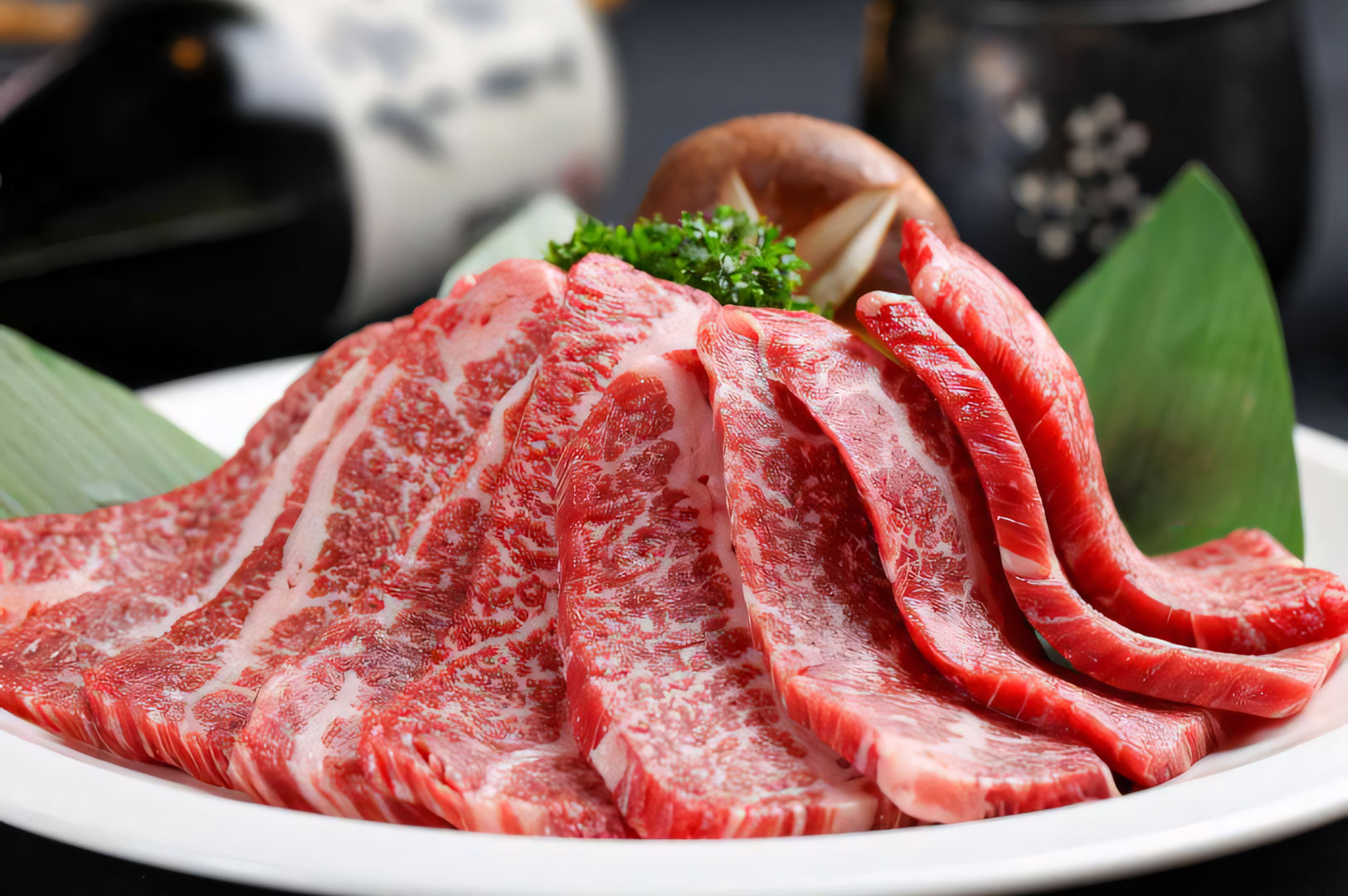 A presentation platter of fresh, thinly sliced marbled beef arranged beautifully with greenery garnish, ready for Japanese BBQ grilling.