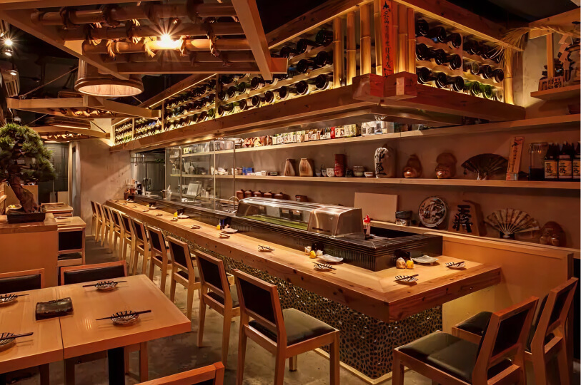 An upscale, warmly lit yakitori restaurant featuring a long wooden counter, intricate bamboo ceiling accents, and shelves lined with sake bottles and traditional decor.