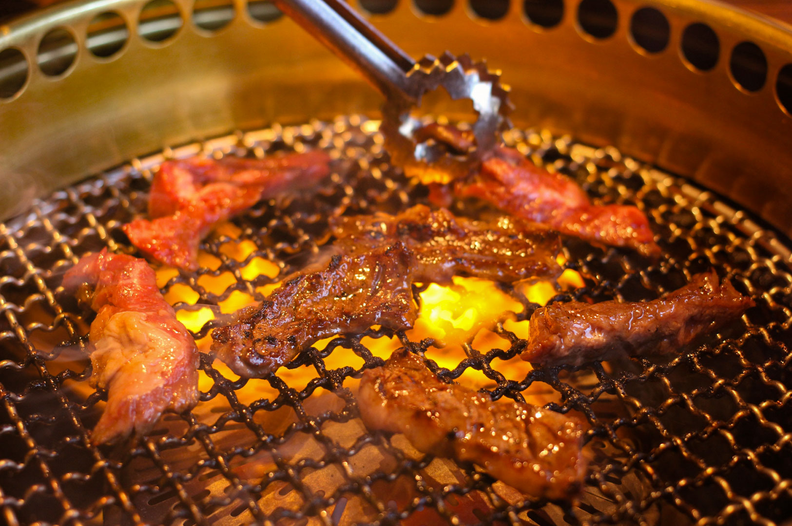 Close-up view of seasoned beef strips sizzling and cooking over an open flame on a wire mesh charcoal grill.