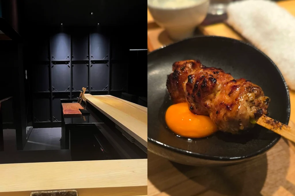 A composite image featuring two contrasting sides. The left side captures a dimly lit, sophisticated high-end Japanese-style interior, characterized by a long, pristine wooden counter bar and traditional black paneled shoji screens adorned with intricate brass hardware. A few chairs are tucked neatly in front of the counter, with overhead spotlights casting dramatic shadows, while the foreground shows a close-up section of another wooden bar edge and a small ceramic plate. In sharp contrast, the right side presents a tight, focused close-up of an expertly grilled yakitori skewer resting in a rustic, dark ceramic bowl. The skewer features perfectly charred, savory tsukune (chicken meatballs) glazed in sauce, with a perfectly formed, vibrant orange-yellow egg yolk dipping well visible beneath the skewered meat. The background remains heavily blurred, showing hints of other wooden table surfaces and white bowls, emphasizing the texture of the charcoal-grilled meat and the richness of the egg yolk.