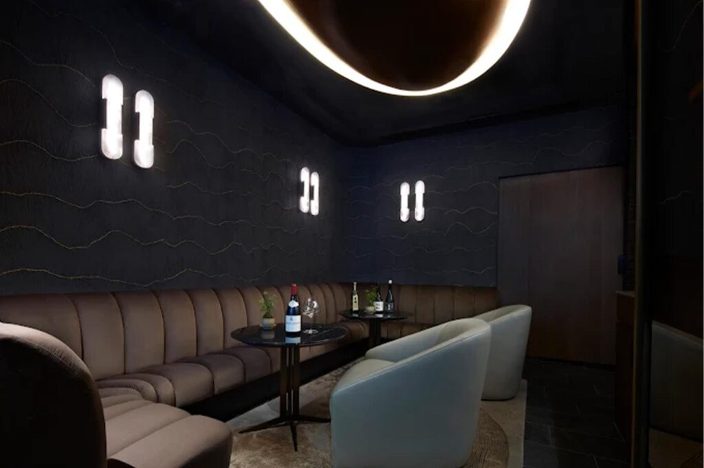 A luxury restaurant lounge area featuring plush curved banquette seating, marble tables, and contemporary glowing wall light fixtures.
