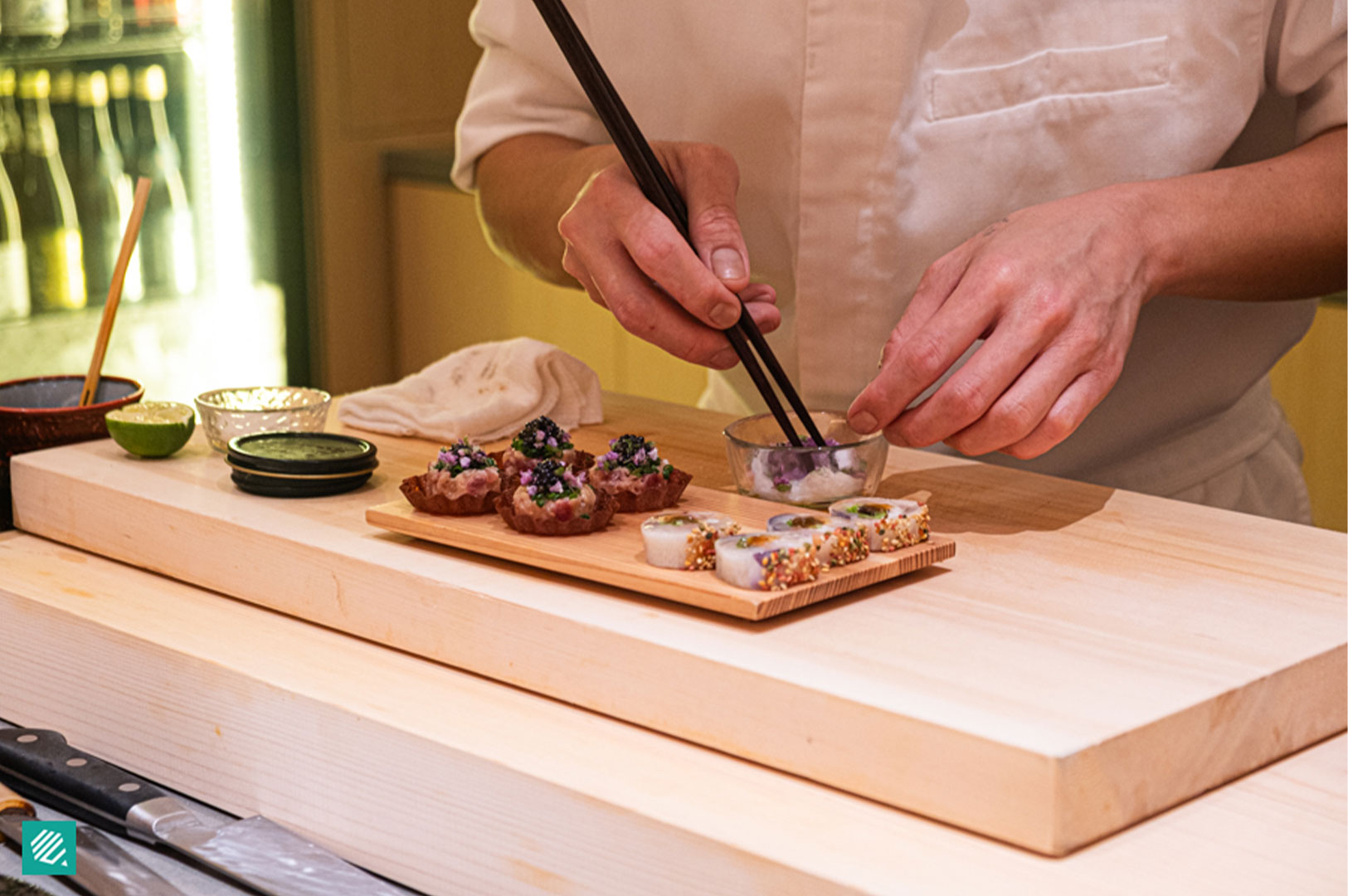 An Omakase chef using chopsticks to meticulously plate delicate appetizers on a wooden serving board.