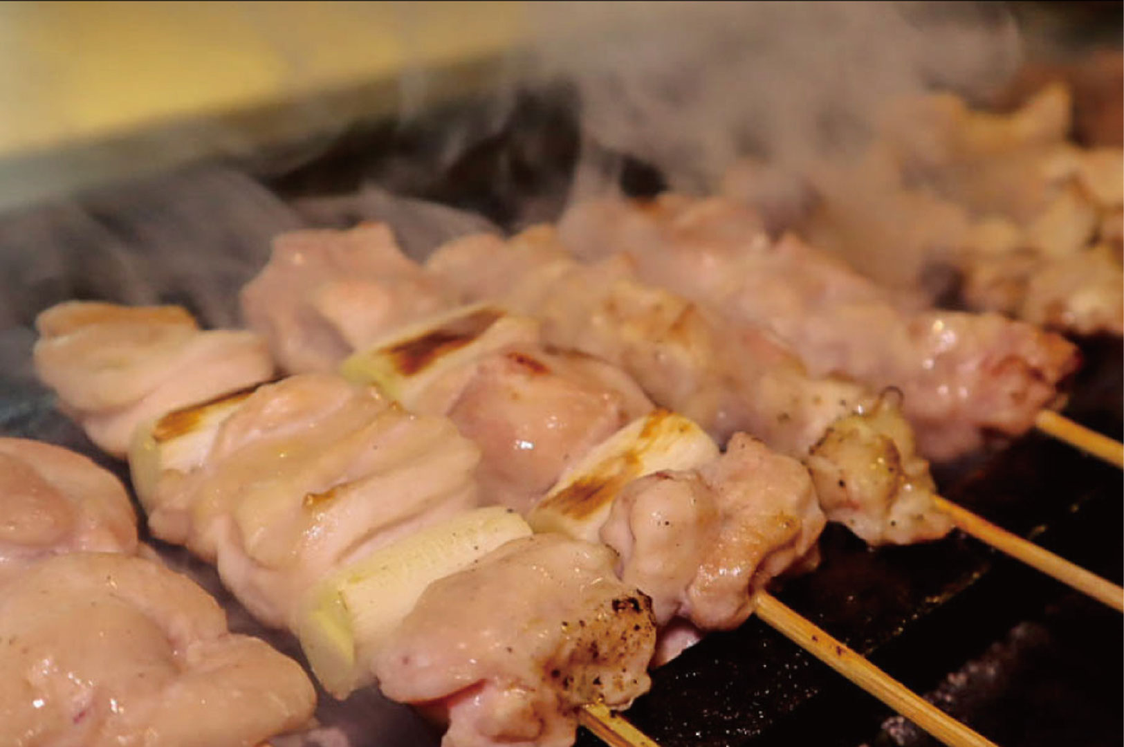Close-up of chicken and onion yakitori skewers steaming on a hot grill at the restaurant.