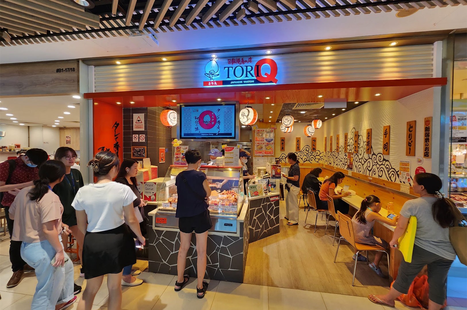 The bright storefront of a Tori-Q Japanese Yakitori outlet in a shopping mall, showing customers queuing to order from the glass display case filled with fresh skewers.