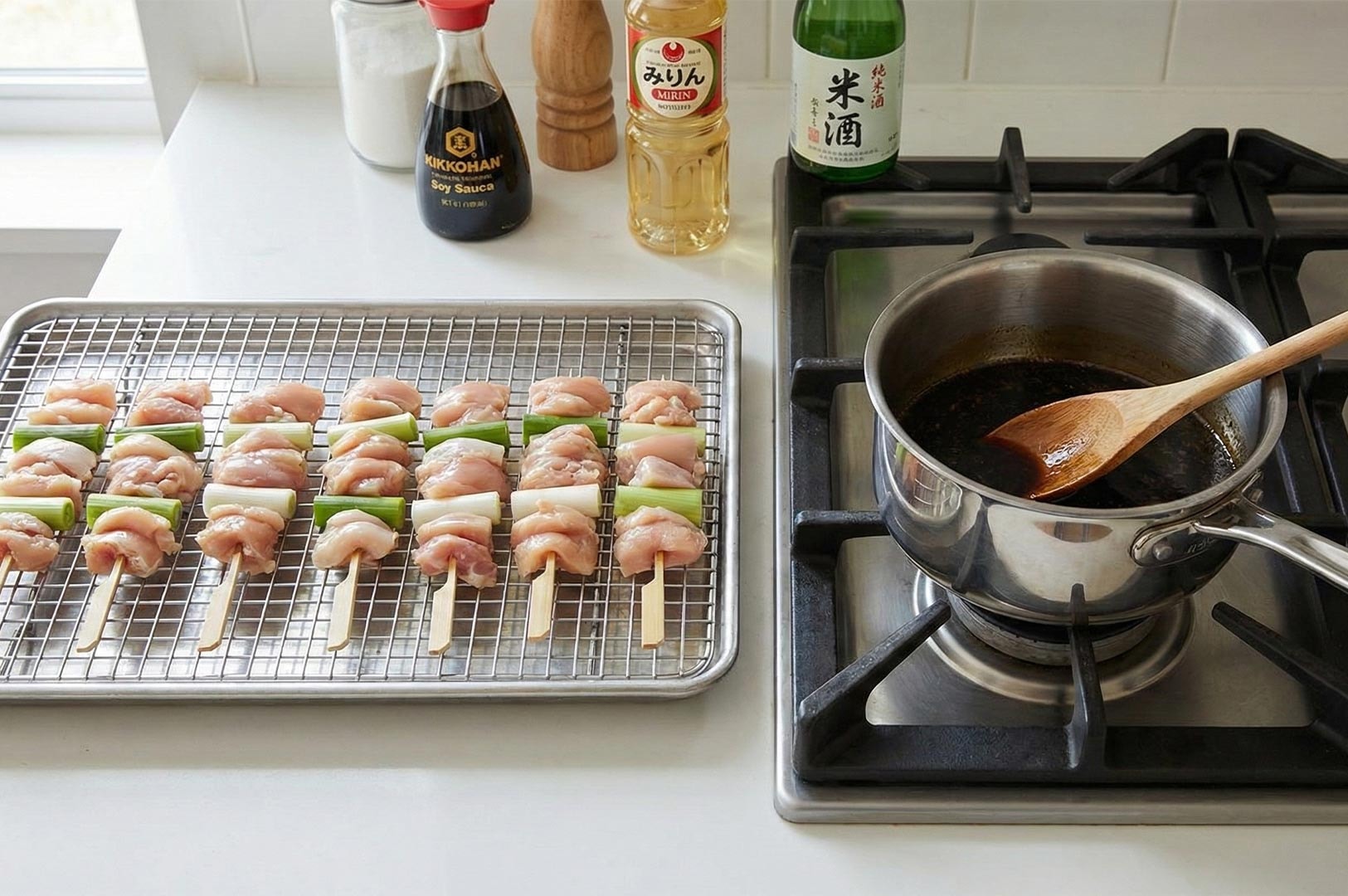 Kitchen setup for homemade yakitori featuring raw chicken and leek skewers (Negima) on a rack, sauce simmering on the stove, and bottles of soy sauce, mirin, and sake.