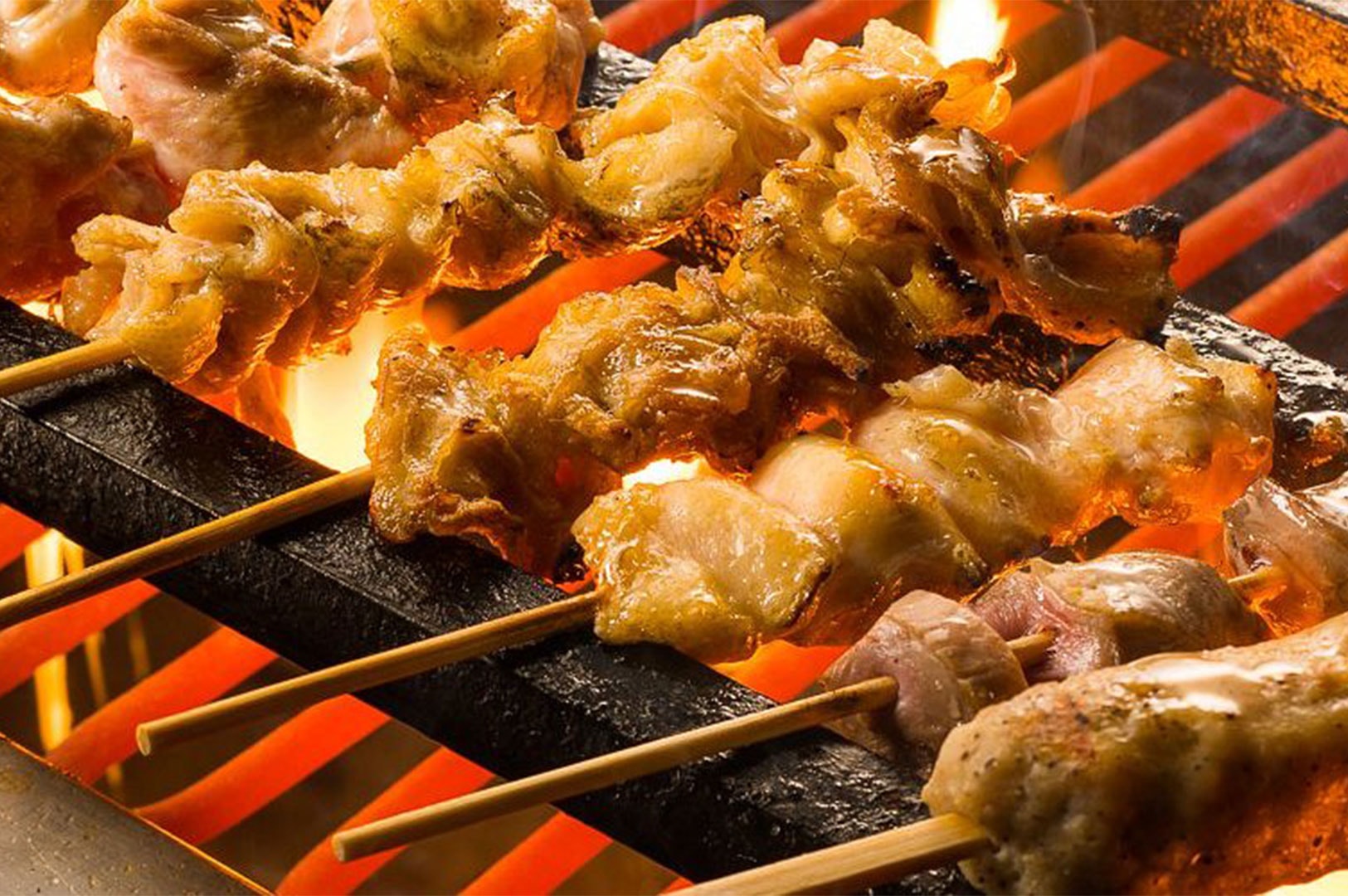 Japanese Yakitori skewers, likely chicken skin (kawa), grilling directly over hot charcoal with visible flames and smoke rising from the cooking process.