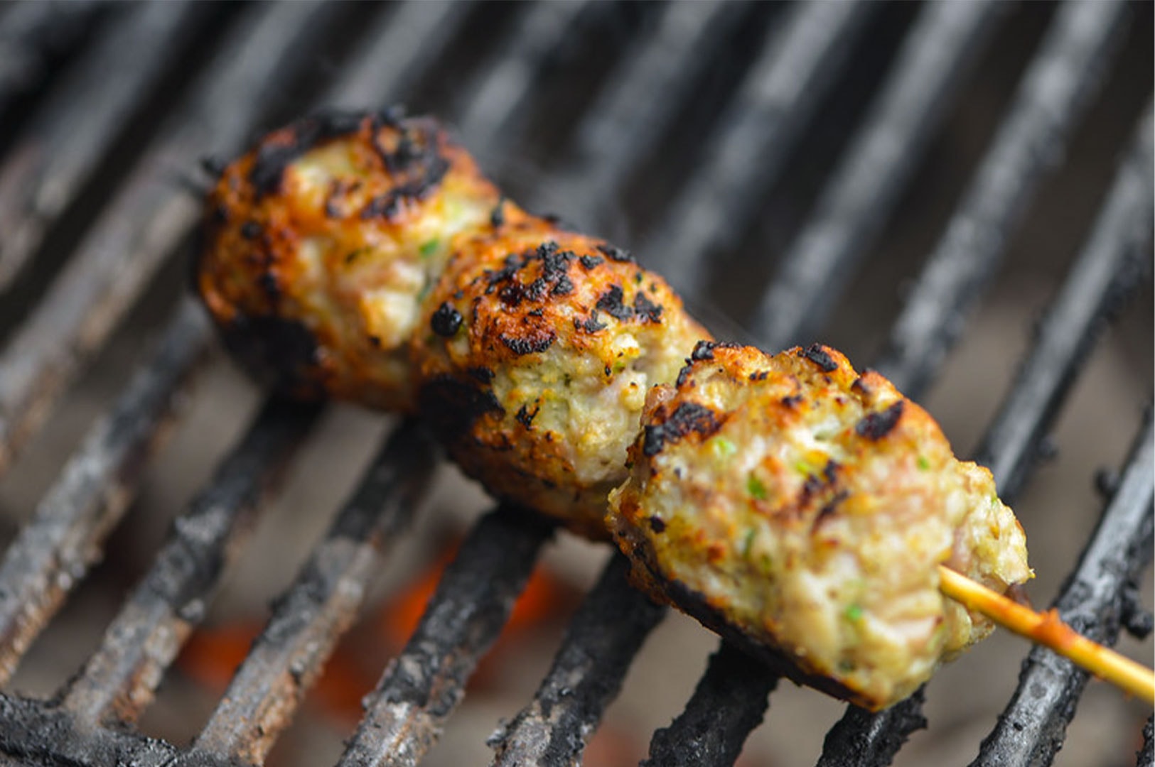 Close-up detail of a Japanese Tsukune chicken meatball skewer cooking on a grill grate, showing char marks and texture.