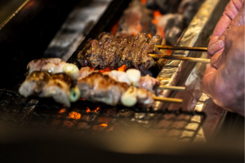 Close-up of a chef’s hands carefully turning chicken skewers over glowing hot charcoal on a traditional Japanese grill.