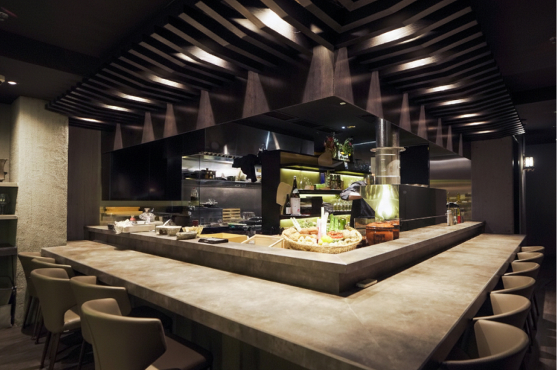 An empty, modern Japanese-style wrap-around dining counter with a dark, architectural slatted ceiling and a central open kitchen area.