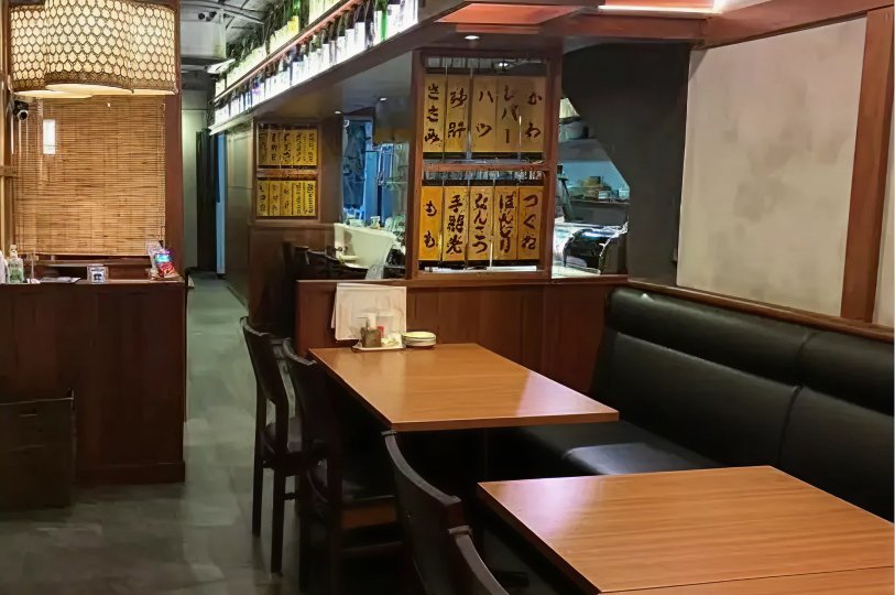 The interior of a cozy, traditional Japanese yakitori restaurant featuring wooden tables, black booths, and menus written on hanging wooden slats.