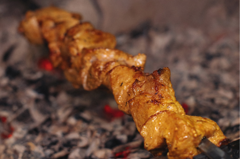 A single chicken skewer cooking directly over glowing hot charcoal embers.