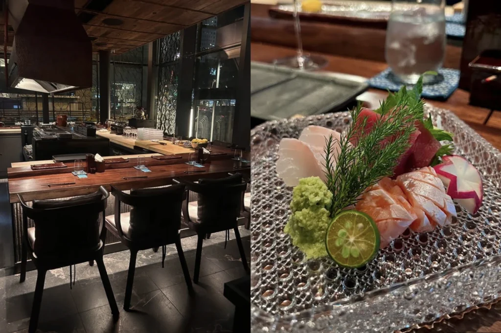 This split-screen image contrasts a moody restaurant interior with a vibrant plate of sashimi. The left side shows a modern, dimly lit Japanese bar with dark wooden counters, high-backed black chairs, and a stainless steel prep station under a large industrial vent. The right side features a close-up of fresh sashimi—including salmon and whitefish—arranged on a clear, bubbly-textured glass plate, garnished with a mound of wasabi, a slice of calamansi lime, and a decorative radish slice.
