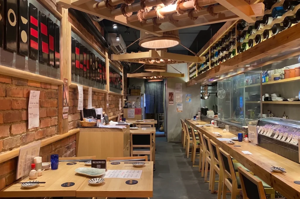 The warm and cozy interior of Yakitori Yatagarasu restaurant featuring wooden tables, brick walls, a long counter bar, and traditional Japanese decor.